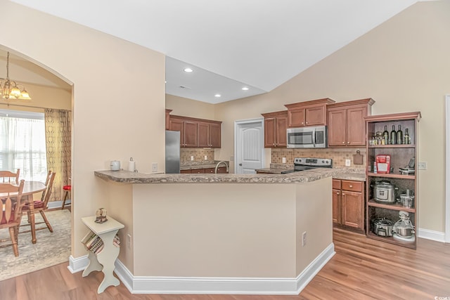 kitchen with lofted ceiling, light wood-style flooring, stainless steel appliances, brown cabinetry, and an inviting chandelier