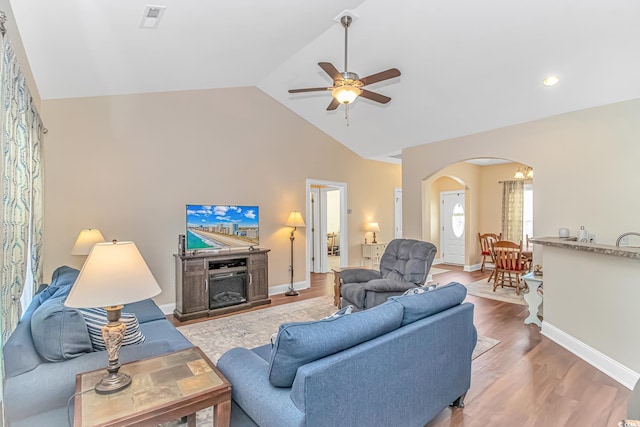 living area with arched walkways, ceiling fan, wood finished floors, vaulted ceiling, and a fireplace