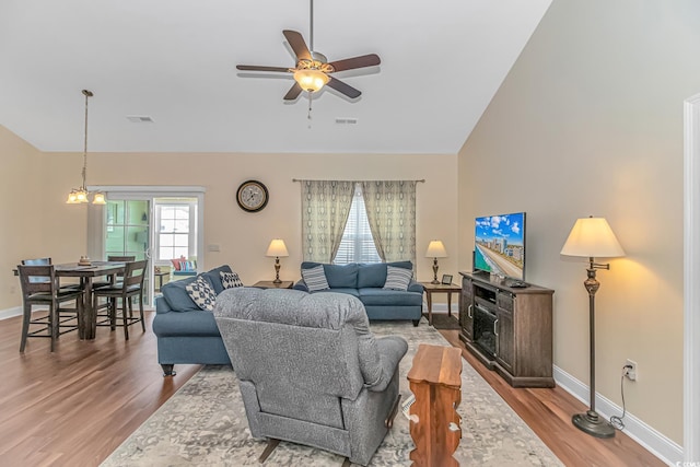 living room featuring ceiling fan with notable chandelier, wood finished floors, visible vents, and baseboards