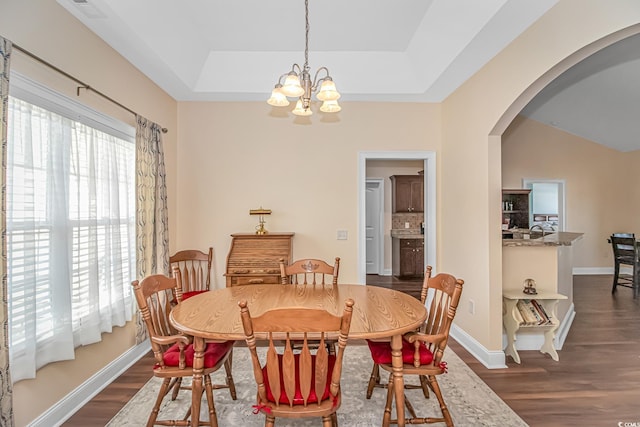 dining area featuring arched walkways, a tray ceiling, plenty of natural light, and dark wood-style floors