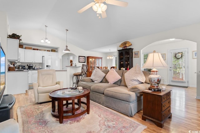 living room with lofted ceiling, ceiling fan with notable chandelier, and light wood-type flooring