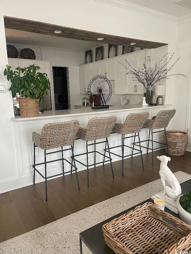 kitchen featuring tasteful backsplash, white cabinetry, a kitchen breakfast bar, ornamental molding, and dark wood-type flooring