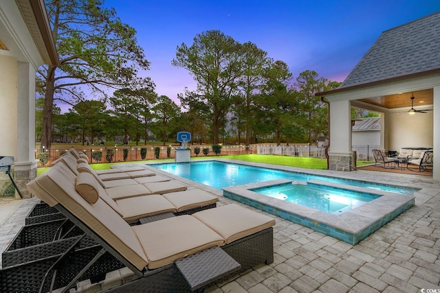 pool at dusk with a patio, ceiling fan, and an in ground hot tub