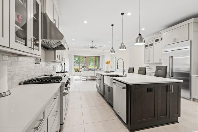 kitchen with sink, high end appliances, white cabinetry, hanging light fixtures, and a center island with sink