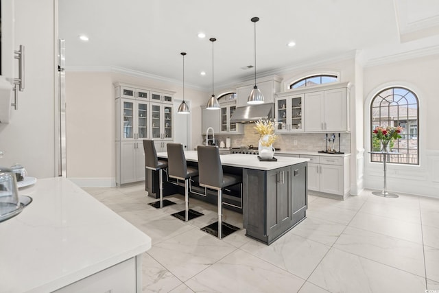 kitchen with pendant lighting, crown molding, a kitchen island with sink, ventilation hood, and decorative backsplash