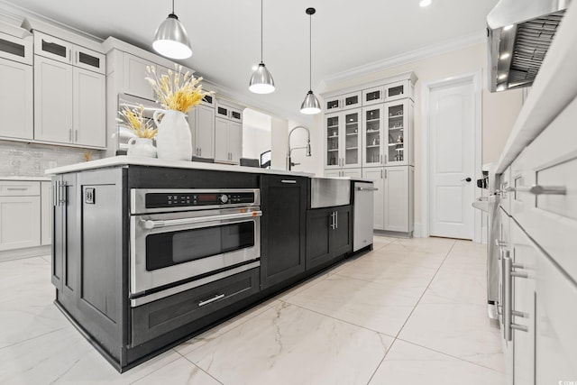 kitchen with pendant lighting, crown molding, an island with sink, white cabinets, and oven