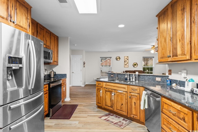 kitchen featuring sink, stainless steel appliances, kitchen peninsula, dark stone counters, and light wood-type flooring