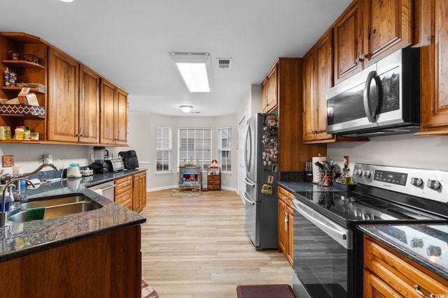 kitchen featuring sink, light hardwood / wood-style floors, dark stone counters, and appliances with stainless steel finishes