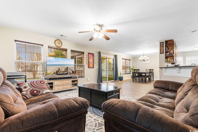 living room with ceiling fan with notable chandelier and light hardwood / wood-style flooring