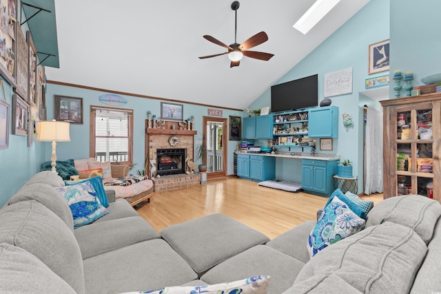 living area with a brick fireplace, built in study area, ceiling fan, light wood-style floors, and high vaulted ceiling