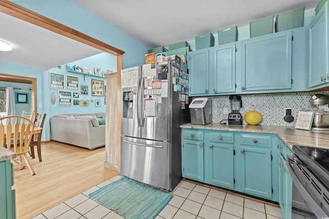 kitchen featuring light tile patterned flooring, black electric range, blue cabinetry, stainless steel refrigerator with ice dispenser, and backsplash