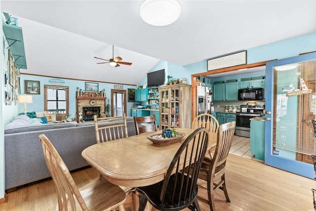 dining room with lofted ceiling, a fireplace, light wood-style flooring, and a ceiling fan