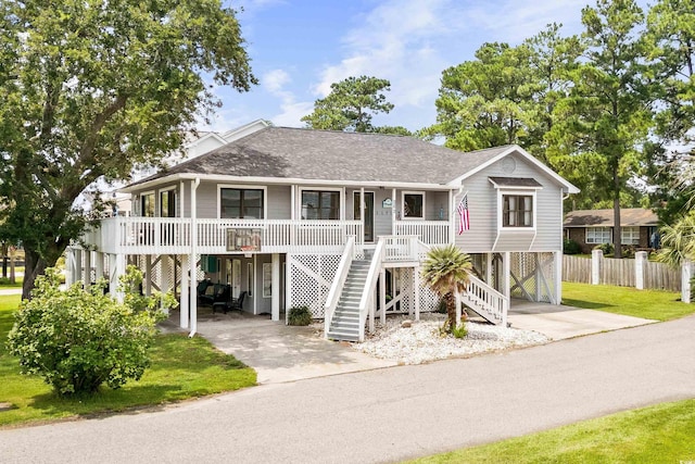 coastal home featuring a porch, a shingled roof, concrete driveway, stairway, and a carport