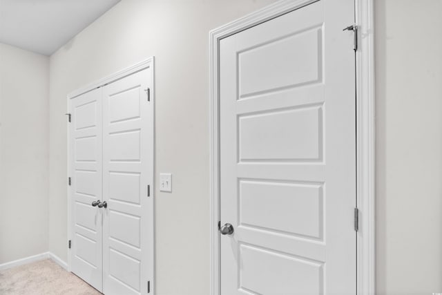 hallway with baseboards and light colored carpet