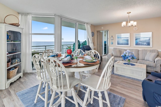 dining space with a notable chandelier, a textured ceiling, a water view, and wood finished floors