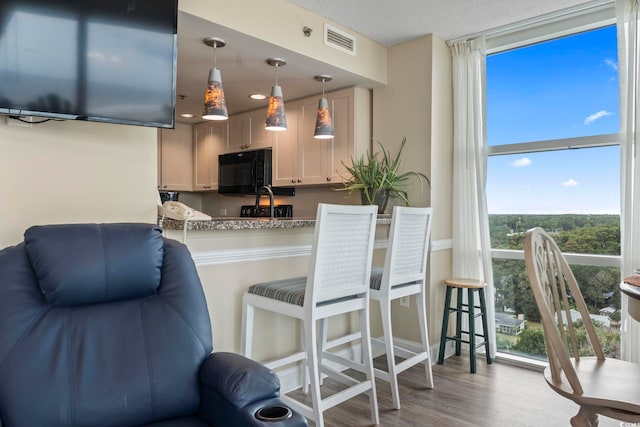 kitchen featuring visible vents, pendant lighting, wood finished floors, a breakfast bar area, and black microwave