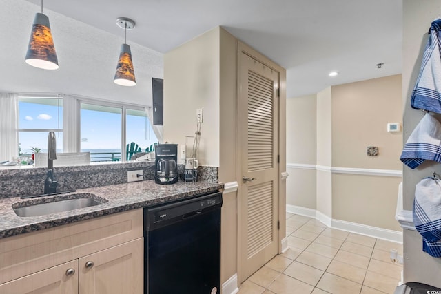 kitchen with dark stone countertops, light tile patterned floors, a sink, dishwasher, and decorative light fixtures