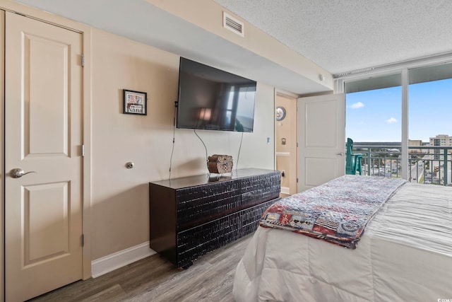 bedroom with a textured ceiling, wood finished floors, visible vents, baseboards, and expansive windows