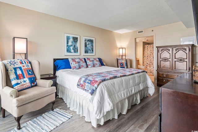 bedroom with visible vents, connected bathroom, a textured ceiling, and wood finished floors