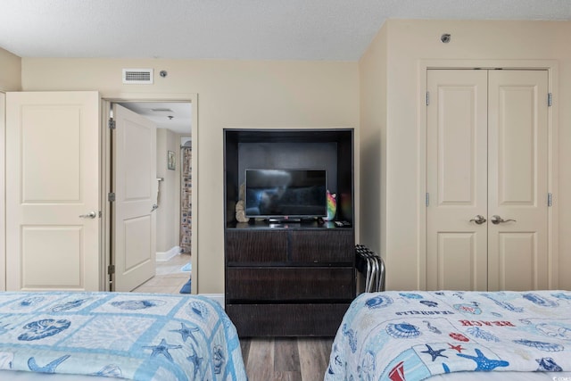 bedroom with wood finished floors, visible vents, a closet, and a textured ceiling