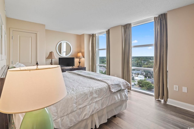 bedroom with a textured ceiling, a wall of windows, baseboards, and wood finished floors