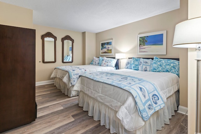 bedroom with a textured ceiling, baseboards, and wood finished floors