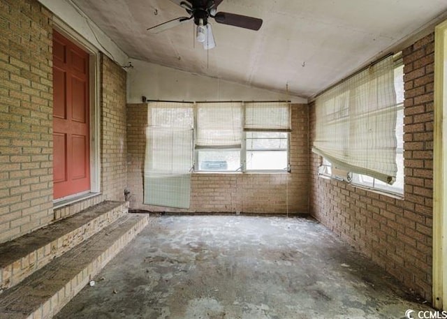 interior space with a ceiling fan, brick wall, and vaulted ceiling