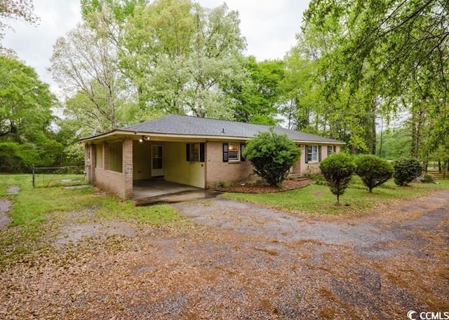 back of house featuring brick siding, aphalt driveway, fence, and a carport