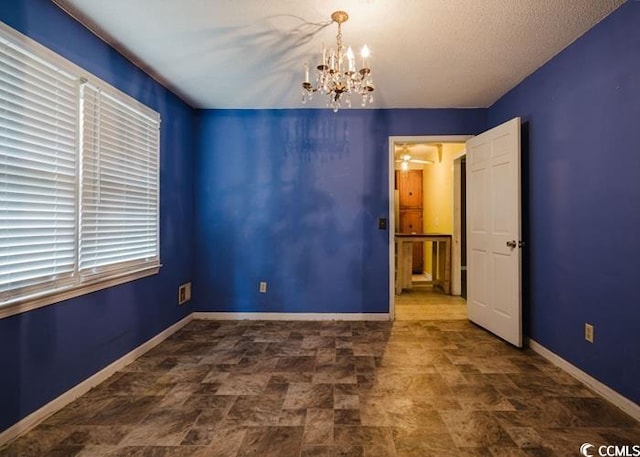 unfurnished room featuring stone finish floor, baseboards, and a notable chandelier
