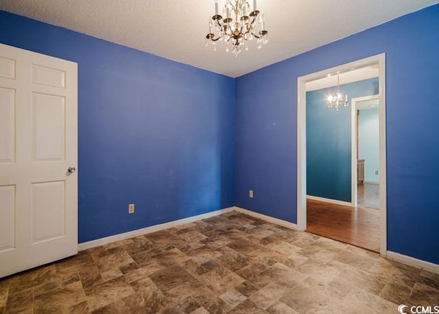 spare room featuring baseboards, a chandelier, and stone finish floor