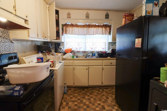 kitchen with dark floors, under cabinet range hood, freestanding refrigerator, washer / clothes dryer, and a sink