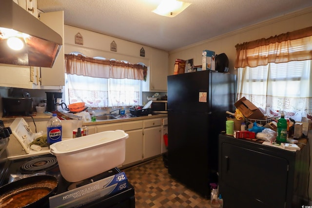 kitchen featuring dark floors, under cabinet range hood, freestanding refrigerator, a textured ceiling, and a sink