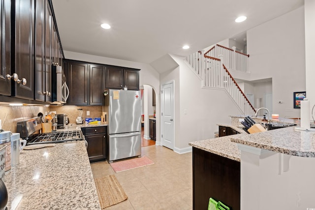 kitchen with appliances with stainless steel finishes, dark brown cabinetry, tasteful backsplash, light stone countertops, and a kitchen bar