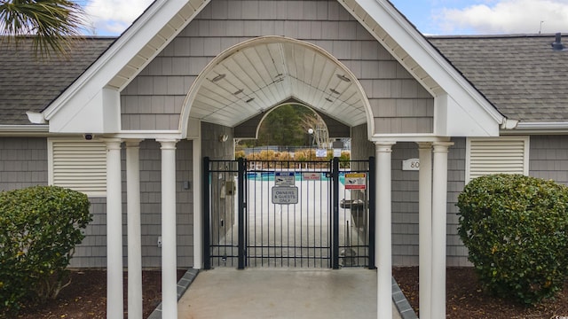 entrance to property featuring a shingled roof, a gate, and fence