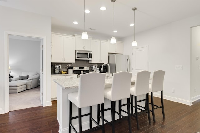 kitchen featuring appliances with stainless steel finishes, white cabinets, decorative light fixtures, and a center island with sink