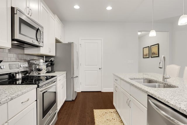 kitchen with white cabinets, appliances with stainless steel finishes, light stone countertops, pendant lighting, and a sink