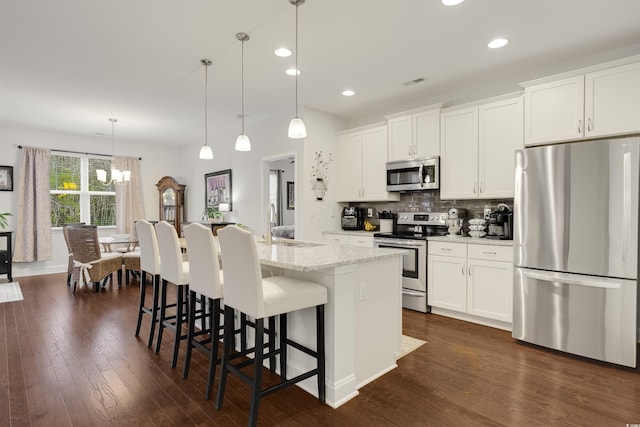 kitchen with an island with sink, light stone countertops, stainless steel appliances, white cabinetry, and pendant lighting