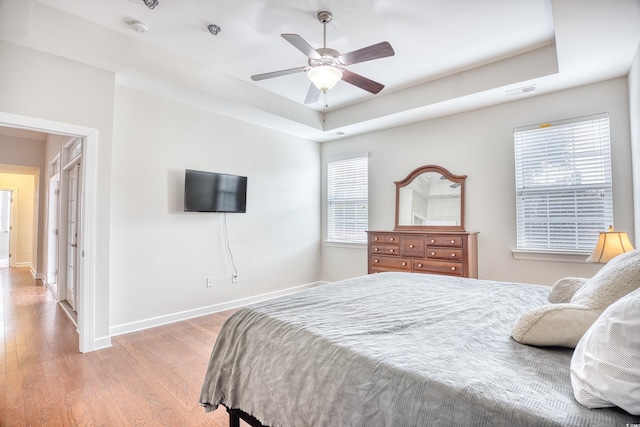 bedroom featuring ceiling fan, a tray ceiling, and light hardwood / wood-style flooring