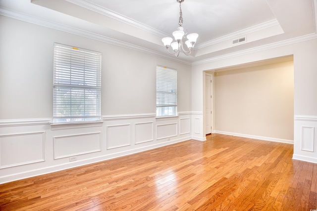 spare room featuring light hardwood / wood-style floors, a chandelier, and a tray ceiling