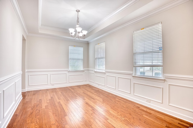 empty room featuring crown molding, a tray ceiling, a chandelier, and light wood-type flooring