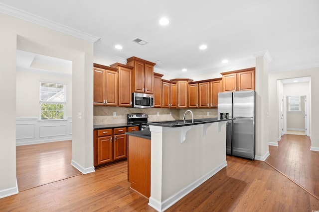 1537 Beaumont Way, Myrtle Beach, SC 29577 - kitchen featuring appliances with stainless steel finishes, dark countertops, light wood-style flooring, a kitchen island with sink, and brown cabinets
