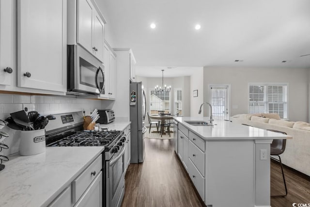 kitchen with a sink, white cabinets, open floor plan, appliances with stainless steel finishes, and a kitchen bar