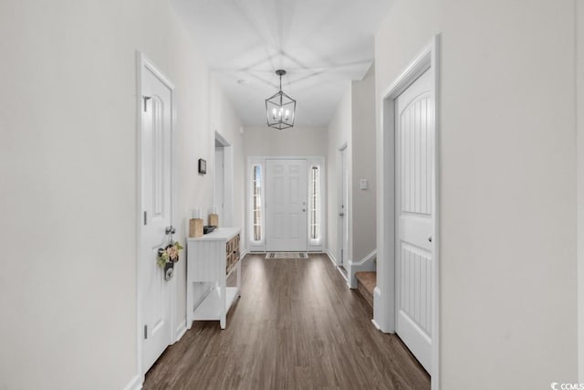 doorway with dark wood-type flooring, an inviting chandelier, and baseboards