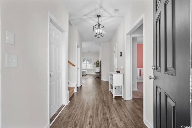 corridor with dark wood-type flooring, a notable chandelier, stairway, and baseboards