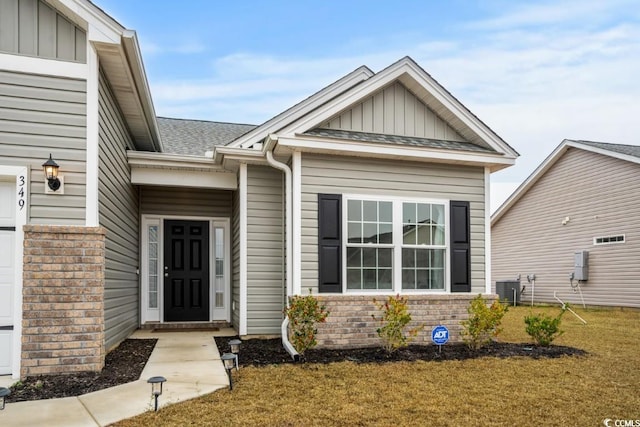 entrance to property with board and batten siding, brick siding, a lawn, and roof with shingles