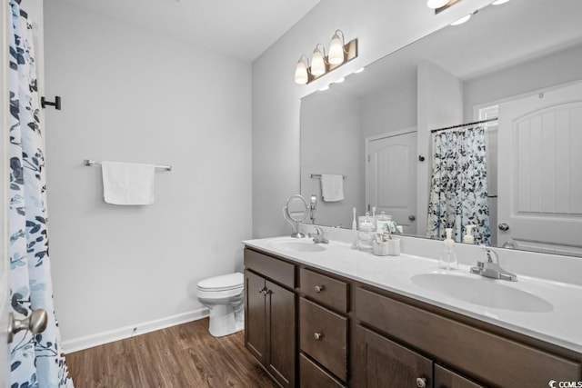 bathroom featuring double vanity, wood finished floors, a sink, and toilet