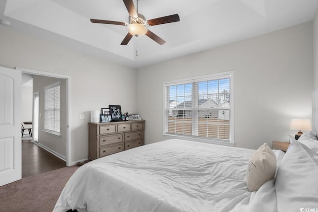 bedroom featuring baseboards, a tray ceiling, dark colored carpet, and a ceiling fan