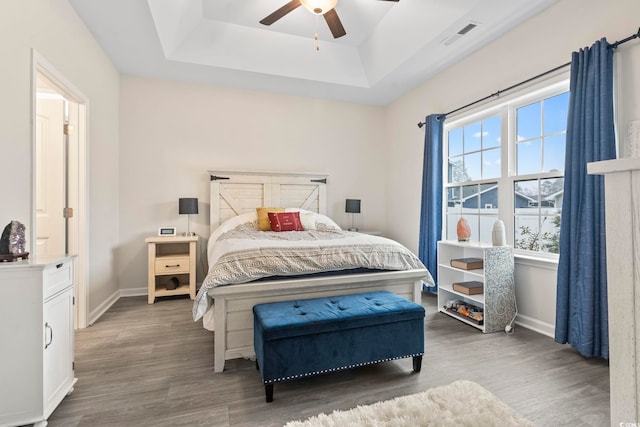 bedroom with dark wood-type flooring, ceiling fan, and a raised ceiling