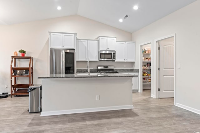 kitchen featuring stainless steel appliances, a center island with sink, dark stone countertops, and white cabinets