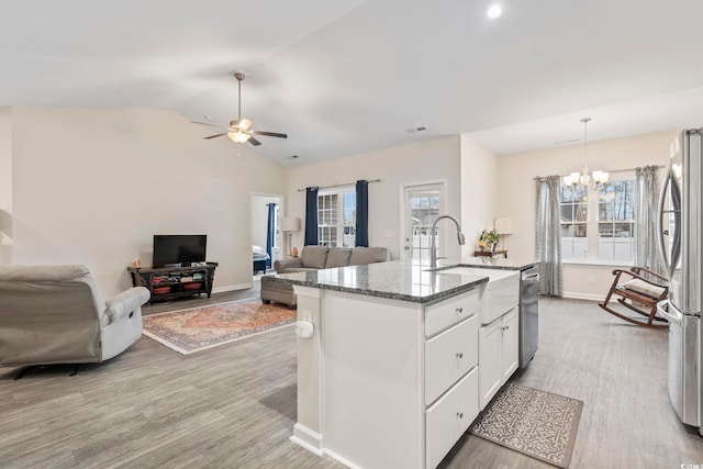 kitchen with appliances with stainless steel finishes, decorative light fixtures, dark stone countertops, white cabinets, and a kitchen island with sink